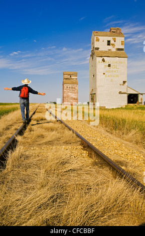 ein Mann Wanderungen entlang der Bahnstrecke mit verlassenen Aufzüge im Hintergrund, Dankin, Saskatchewan, Kanada Stockfoto