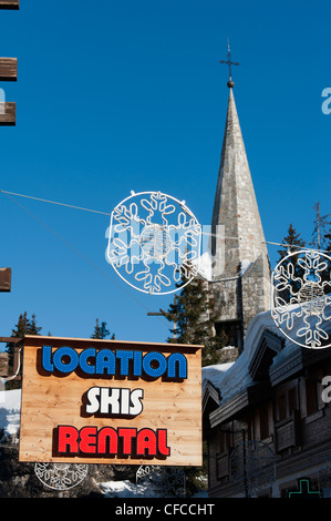 Ski Verleih Shop anmelden mit Courchevel 1850 Kirche und Straßen mit Dekorationen aufgereiht auf der anderen Straßenseite. Stockfoto