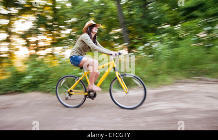 eine junge Frau fährt ein gelben Fahrrad auf einem Feldweg. Stockfoto