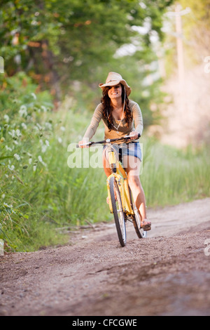 eine junge Frau fährt ein gelben Fahrrad auf einem Feldweg. Stockfoto