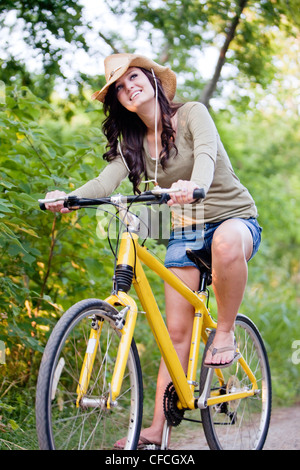 Eine lächelnde junge Frau Fahrradtouren gelb auf einem Feldweg. Stockfoto