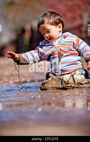 ein zweier Jahre alter Junge spielt in einer Pfütze. Stockfoto