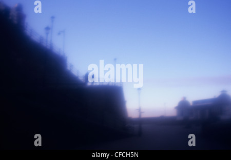 Atmosphärische Ansicht der Figuren am Hang oberhalb der Strandpromenade und Seebrücke Silhouette gegen den Abendhimmel Stockfoto