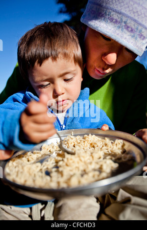 ein Junge sitzt auf seinem Schoß Mütter während sie Nudeln im Hinterland Essen. Sie sind am Squaw Pass lagerten. Stockfoto