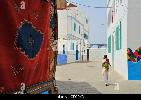 Teppich und Frau mit einem Baby auf ihr zurück in die alte Stadt Asilah, Atlantikküste, Marokko, Afrika Stockfoto