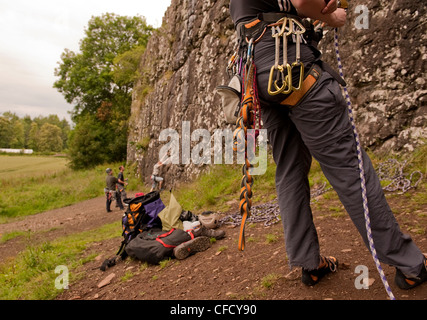 Ein Bergsteiger begibt sich auf eine Sport-Route, dass Benny Beg, Schottland, während eine andere sichernde und Ausrüstung stehen im Vordergrund Stockfoto