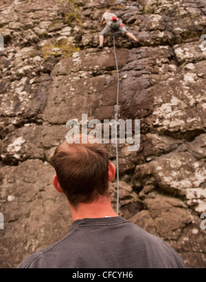 Die Rückseite des Kopfes eine sichernde Uhren eine Kletterpflanze, die bis einen nassen Patch einer Sport-Route mit einem Seil an Benny Beg, Schottland reisen Stockfoto