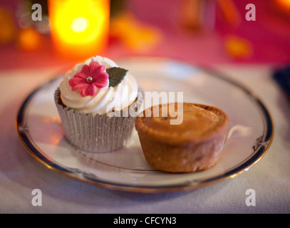 Eine Tasse Kuchen und Torte sitzen auf einem Teller, beleuchtet von einer Kerze mit flachen Fokus bei einer Hochzeit Stockfoto