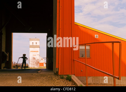 Ein Mann hält eine Schaufel blickt auf eine alte Kornlift, Kincaid, Saskatchewan, Kanada Stockfoto