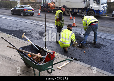 Drei Arbeiter die Straßenoberfläche reparieren Schäden mit Schlaglöchern und Wasser Erosion, Glasgow, Schottland, Großbritannien Stockfoto