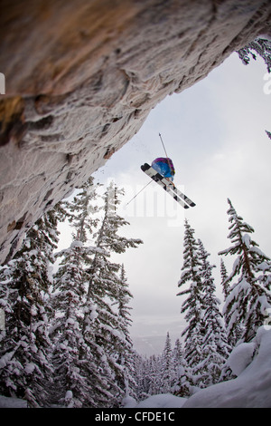 Ein junger männlicher Skifahrer fällt einem großen Felsen am Kicking Horse Resort, Golden, Britsh Columbia, Kanada Stockfoto