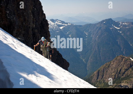 Zwei Bergsteiger steigen ein Snowpatch auf dem Weg an die Spitze der Elkhorn Mountain im Strathcona Park, Vancouver Island, Kanada. Stockfoto