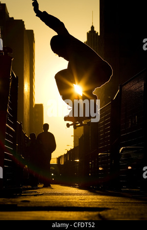 Ein Skateboarder tut ein "Ollie" entlang einer Straße in der Innenstadt von Toronto bei Sonnenuntergang, Ontario, Kanada. Stockfoto