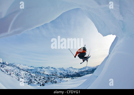 Eine junge männliche Freeskier springt ein Gesims und Skitouren in den Monashee Mountains, British Columbia, Kanada Stockfoto