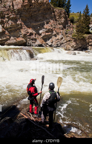 Zwei männliche Wildwasser-Kajakfahrer scout die Wasserfälle am Oldman River, Alberta, Kanada Stockfoto