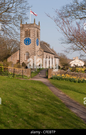 Eingang Gateway Arch, Narzissen im Kirchhof & historische, malerische St. Peter's Kirche unter blauem Himmel im Frühjahr - Addingham, Yorkshire, England, UK. Stockfoto