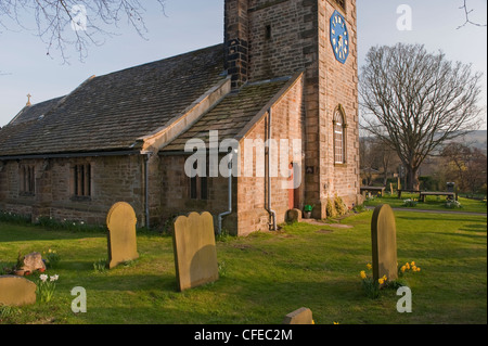 Das malerische St. Peter's Kirche mit Uhr auf Turm, Narzissen und Grabsteine in Kirchhof-sonnigen Frühling Abend, Addingham Dorf, Yorkshire, England. Stockfoto