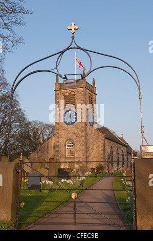 Eingang Gateway Arch, Narzissen im Kirchhof & historische, malerische St. Peter's Kirche unter blauem Himmel im Frühjahr - Addingham, Yorkshire, England, UK. Stockfoto