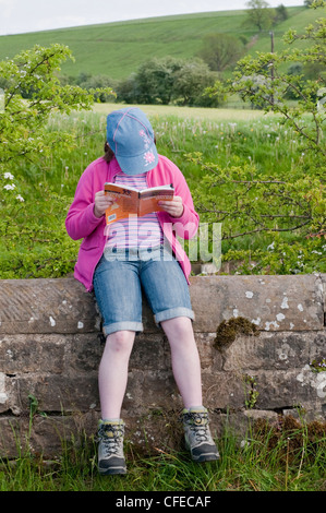 Die malerische Landschaft zu Fuß - junge Mädchen (in Stiefeln) auf Feld Wand saß, Buch & lesen Wanderweg Wegbeschreibung - North Yorkshire, England, UK. Stockfoto