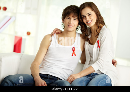 Kippen Sie nach oben jungen lächelnd Paares tragen rote Schleifen darauf hinweist, ihre Unterstützung und das Bewusstsein für AIDS-problem Stockfoto