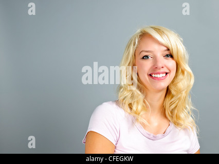 Porträt von lächelnden jungen blonden kaukasischen Frau auf grauem Hintergrund Stockfoto