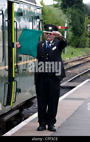 Ein Zug-Wächter bläst seine Pfeife und Wellen seine grüne Flagge für die Ausreise im Toddington Railway Centre in gepflegtes, Großbritannien Stockfoto