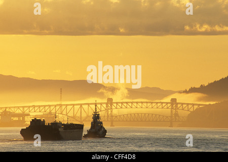 Schlepper mit Barge nähert sich die Eisen Arbeiter Second Narrows Bridge bei Sonnenaufgang, Vancouver, Britisch-Kolumbien, Kanada. Stockfoto