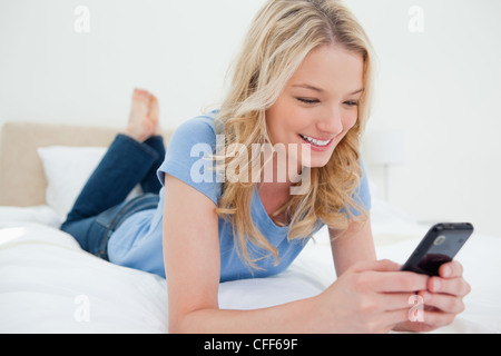 Frau auf dem Bett liegend mit ihrem Smartphone in der hand lächelnd Stockfoto