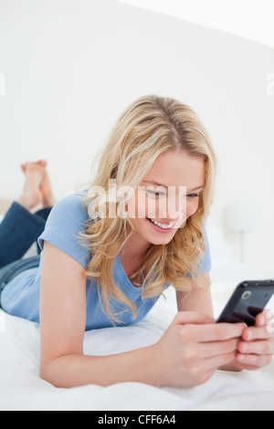 Nahaufnahme, Frau liegend auf einem Bett mit ihrem Smartphone und lächelnd Stockfoto
