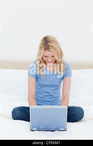 Frau, sitzen, Beine gefaltet vor ihrem Laptop und lächelnd Stockfoto