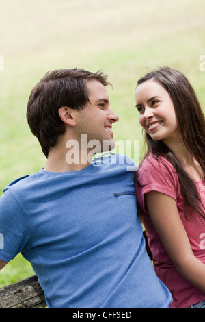 Junge lächelnde paar sahen einander sitzen nebeneinander Stockfoto