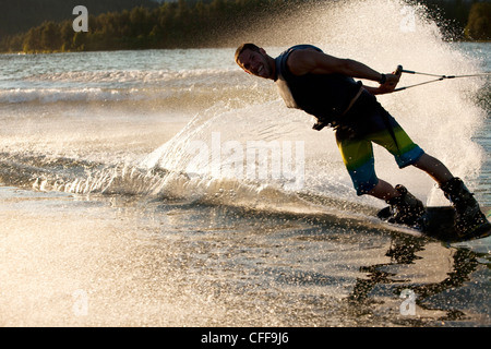 Ein professioneller Wakeboarder lächelt, während er schnitzt und Schrägstriche am Lake Pend Oreille bei Sonnenuntergang in Sandpoint, Idaho. Stockfoto