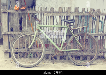 Papaya-Fahrrad-Sri Lanka - ein grünes Fahrrad lehnt sich an einem Zaun mit Papaya und blauer Stuhl im Hintergrund Stockfoto