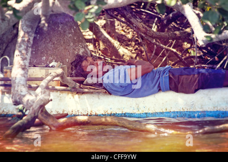 Fischer-ruhen-Koggala-See - ein Fischer ruht im Schatten liegend auf seinem Boot unter einigen Bäumen in Sri Lanka Stockfoto