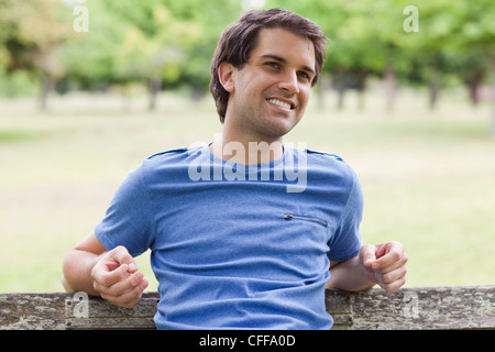 Junger lächelnder Mann sitzen auf einer Bank Stockfoto