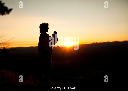 Ein junger Mann, der betet, wie die Sonne erhebt sich über einem Tal in Idaho. Stockfoto