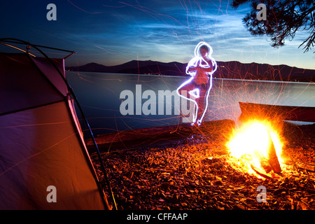 Eine leichte Bild von einer Frau, die beim Yoga neben ihrem Zelt und Lagerfeuer auf einer kampierenden Reise entlang den Ufern eines Sees in Idaho. Stockfoto