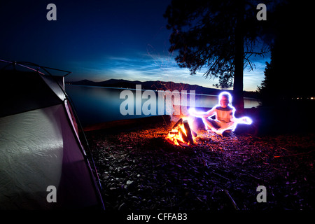 Lightpainting eines Mannes, der neben seinem Zelt und Lagerfeuer auf einer kampierenden Reise entlang den Ufern eines Sees in Idaho zu meditieren. Stockfoto