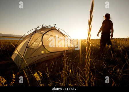 Ein Mann steht neben seinem Zelt bei Sonnenuntergang auf einer Rucksacktour in den Bergen von Montana. Stockfoto