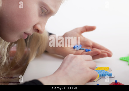 Kleines blondes Mädchen mit Hama-Perlen zu spielen Stockfoto