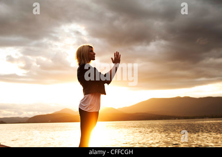 Eine schöne junge Frau als die Sonnenuntergänge über einen See in Idaho zu meditieren. Stockfoto