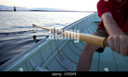 Ein junger Mann-Zeilen in einem Peapod Jolle bei Sonnenuntergang entlang der Küste von Maine in der Nähe von Boothbay Harbor. Stockfoto