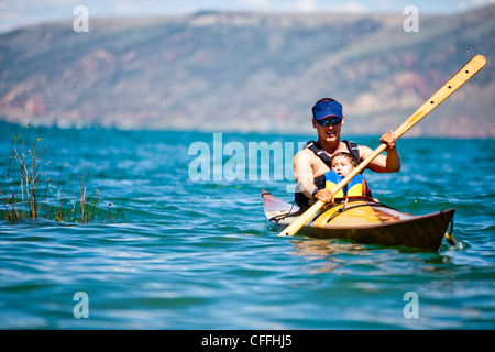 Ein Mann paddelt eine Holz-Kajak mit ein 3 Jahre alter Junge sitzt auf seinem Schoß, Bear Lake. Stockfoto