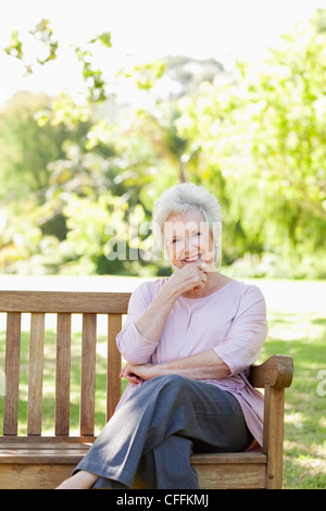 Bei einer Rast den Kopf auf ihre Hand, als sie auf einer Bank sitzt lächelnde Frau Stockfoto