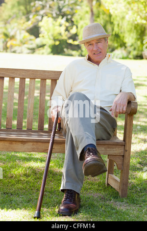 Mann lächelnd bei der Standortwahl auf einer Bank, als er einen Stock halten Stockfoto