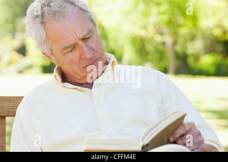 Mann liest ein Buch auf einer Bank sitzend Stockfoto