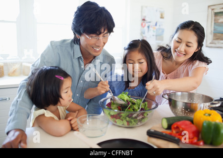 Mutter und Tochter werfen den Salat als der Vater und andere Tochter Stockfoto