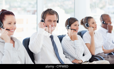 Call-Center-Agenten sitzen zwischen seinen Kollegen lächelnd Stockfoto