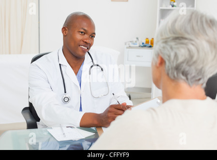 Lächelnde Arzt ist Notizen während seines Patienten spricht Stockfoto