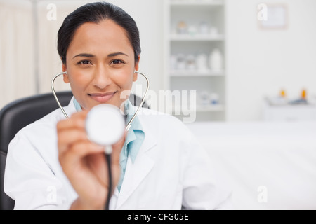 Lächelnde Arzt hält ihr Stethoskop beim Sitzen in ihrem Büro Stockfoto